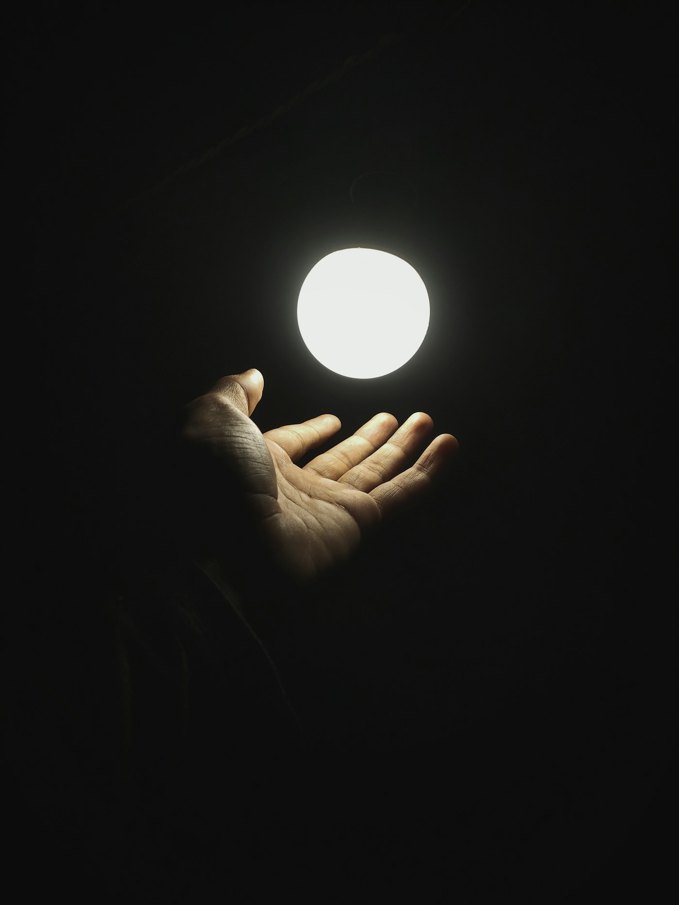 A hand reaching towards a single glowing point of light in the dark
